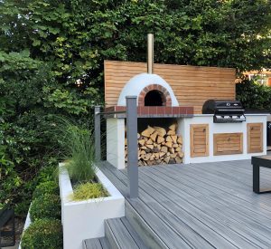 Grey Trex deck with grey timber and aluminium railings, surrounding a wood fired pizza oven and BBQ